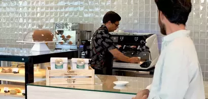Camarero preparando un café y un chico sentado en la barra de la cafetería
