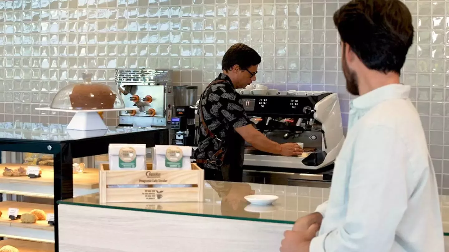 Camarero preparando un café y un chico sentado en la barra de la cafetería