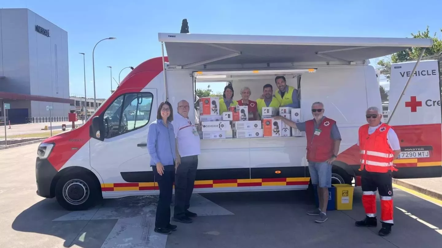 Representantes de Cruz Roja y Nestlé posan junto a un vehículo de reparto con cajas de producto donadas