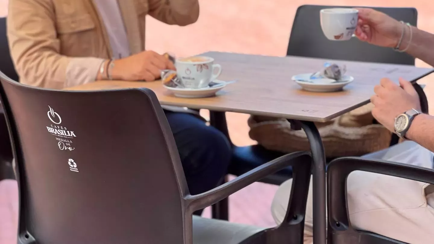 Personas tomando café en una terraza con sillas fabricadas a partir de cápsulas usadas y posos de café.