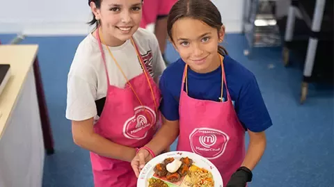 Dues nenes ensenyant un plat en un campament MasterChef